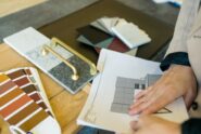 A designer reviewing samples for a kitchen design, with cabinet color swatches and gold handles on a table.
