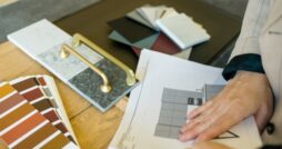 A designer reviewing samples for a kitchen design, with cabinet color swatches and gold handles on a table.