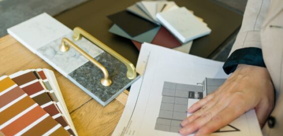 A designer reviewing samples for a kitchen design, with cabinet color swatches and gold handles on a table.