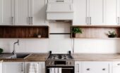 Bright contemporary kitchen featuring white cabinetry, open wood shelving, a gas stove, and minimalist decor.