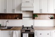 Bright contemporary kitchen featuring white cabinetry, open wood shelving, a gas stove, and minimalist decor.