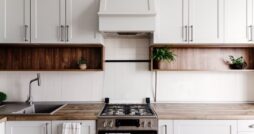 Bright contemporary kitchen featuring white cabinetry, open wood shelving, a gas stove, and minimalist decor.