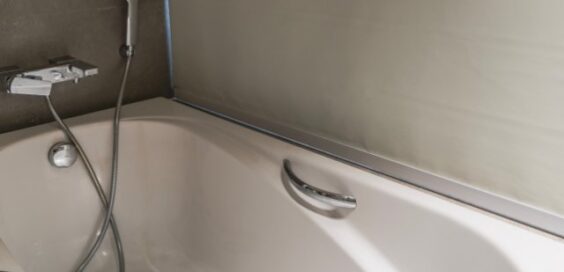 Light shining on a rectangular acrylic bathtub in a residential bathroom. A shower head attachment is on the wall.