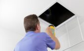 A technician shines a flashlight into an open ceiling air vent while inspecting a home's HVAC ductwork.