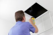 A technician shines a flashlight into an open ceiling air vent while inspecting a home's HVAC ductwork.