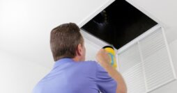 A technician shines a flashlight into an open ceiling air vent while inspecting a home's HVAC ductwork.
