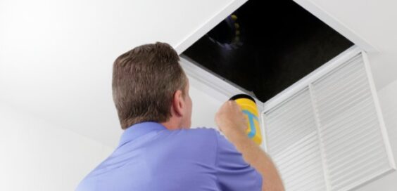 A technician shines a flashlight into an open ceiling air vent while inspecting a home's HVAC ductwork.