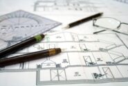 A close-up of the architectural design plans for a home with multiple pens, measuring tools, and eyeglasses on it.
