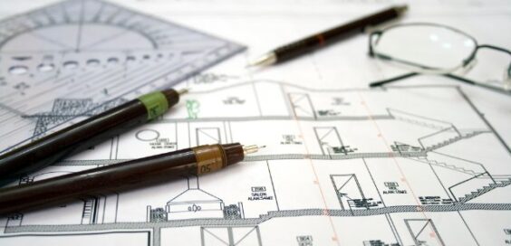 A close-up of the architectural design plans for a home with multiple pens, measuring tools, and eyeglasses on it.