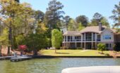 A waterfront home sits among mature trees with a landscaped lawn and private dock extending into the lake.