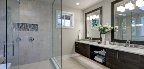 A gray bathroom with a white freestanding tub, glass shower, double sink vanity, large window, and tiled floor.