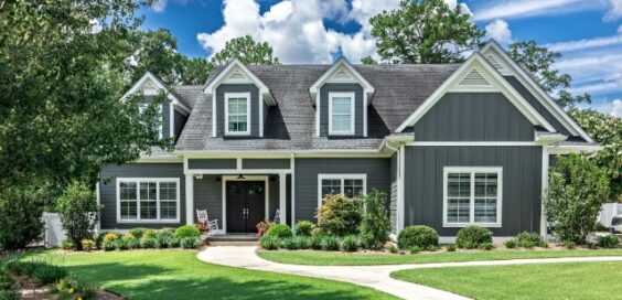 A large dark gray house with white trim, dormer windows, a covered porch, and a curved walkway across a green lawn.