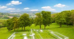An open plot of land with a few trees near the back. There is a floating outline of a house that is to be built on the land.