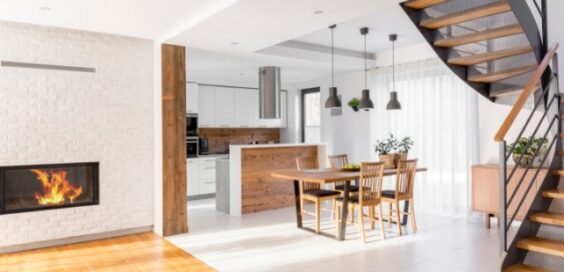 Modern open-plan home with a wood and metal staircase, white brick fireplace, wooden dining table, and bright kitchen.